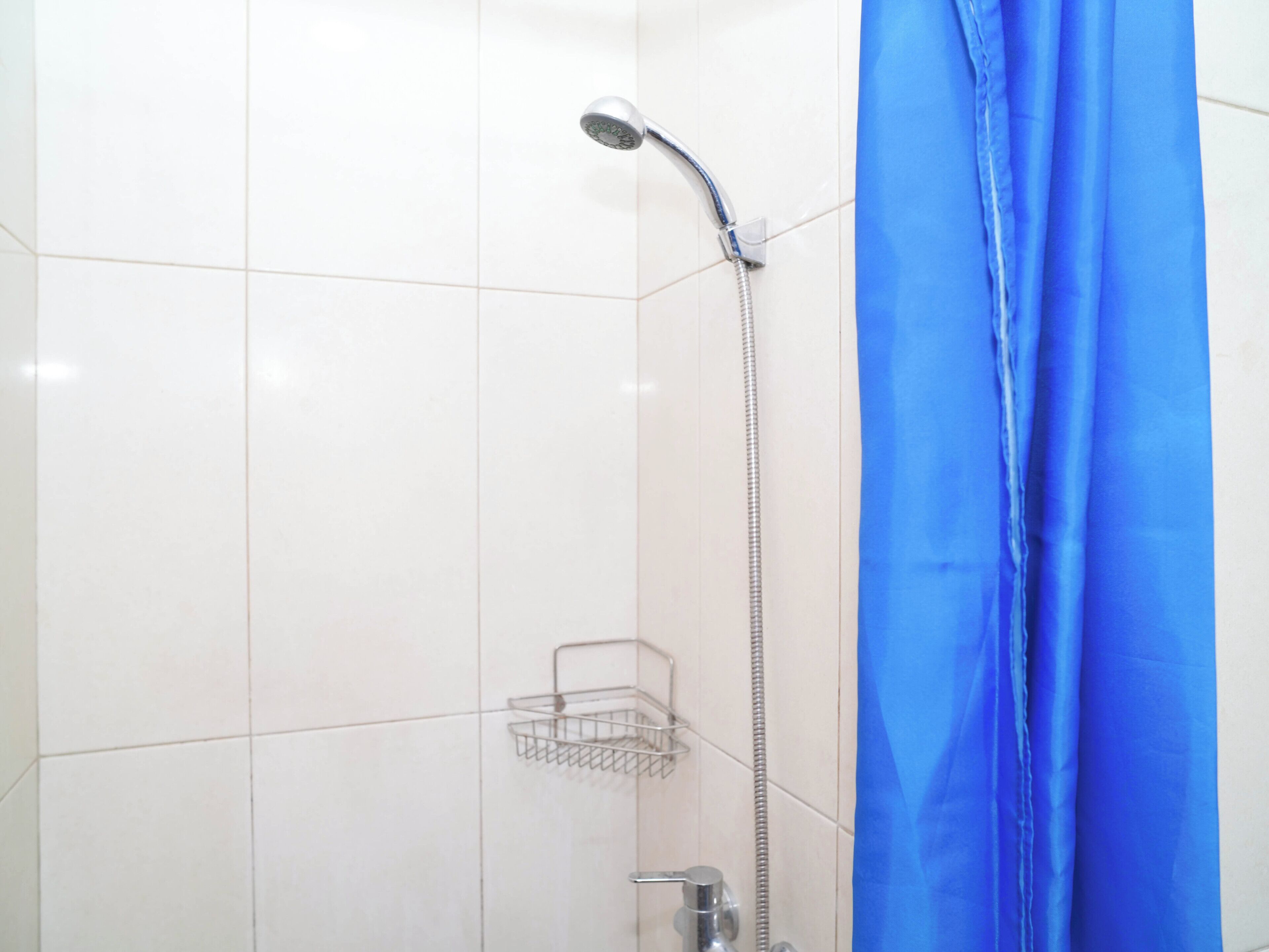 A shower with a blue curtain, a metal shower head, and a metal shelf.