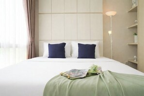 A hotel room with a bed, two pillows, a bedside lamp, a green throw, and a magazine on the bed. - Practical 2Br For 3 Pax At Asatti Apartment (Pagedangan)