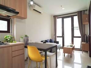 A modern kitchen with a dining area, a sofa, and a small table with a plant. - Practical 2Br For 3 Pax At Asatti Apartment (Pagedangan)