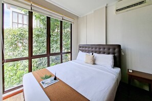 Ein Hotelzimmer mit einem großen Fenster, einem Bett mit weißer Bettwäsche, einem braunen Kopfteil und einem kleinen Nachttisch.
