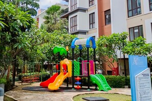 Ein Spielplatz mit Rutschen und Klettergerüsten, umgeben von Grünflächen und einem Gebäude im Hintergrund.