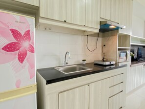 A kitchen with a stainless steel sink, a small potted plant, and a Sharp refrigerator. - Cozy And Roomy Studio Space At Apartment Azalea Suites (Cikarang)
