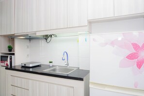 Uma cozinha moderna com armários brancos, uma pia de aço inoxidável, um micro-ondas e um pequeno vaso de planta.