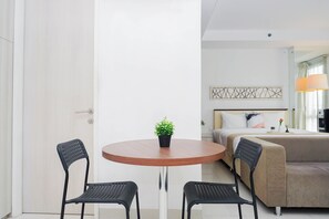 A hotel room with a bed, a sofa, a round table with two chairs, and a potted plant. - Clean And Relaxing Studio Room At Apartment Azalea Suites (Cikarang)