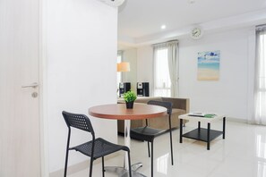 Quarto de hotel moderno com uma mesa de jantar redonda, duas cadeiras pretas, uma pequena planta em vaso, um sofá, uma mesinha de apoio e um quadro na parede.