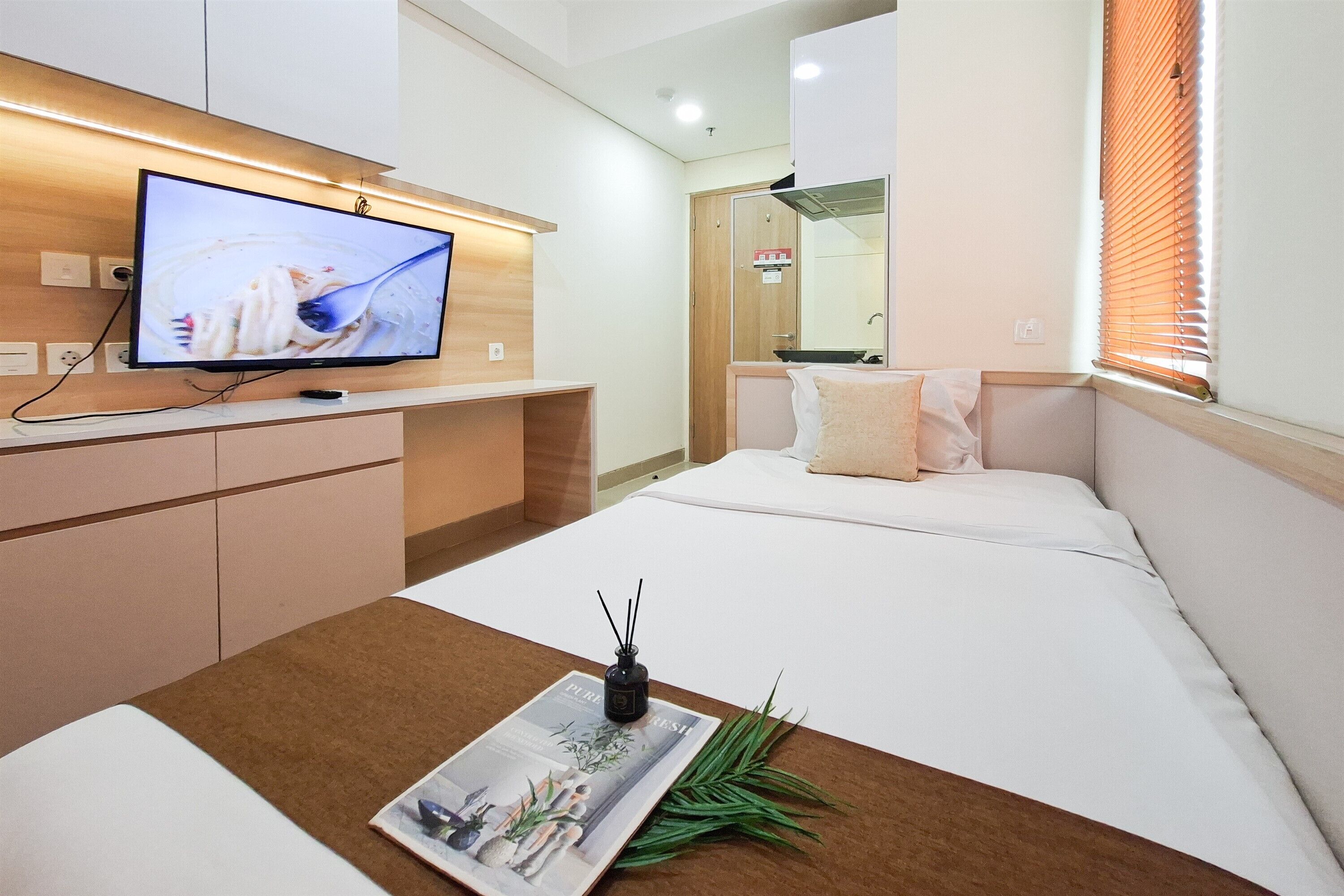 A hotel room with a bed, a TV on a stand, a magazine, and a plant.
