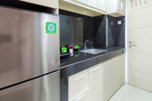 A kitchen with a stainless steel refrigerator, a black countertop, a sink, and light-colored cabinets. - Comfy White Studio For 2 Pax At Bale Hinggil Apartment (Surabaya)