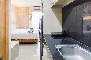 Habitació d'hotel senzilla amb llit, taula de nit i zona de cuina equipada.
