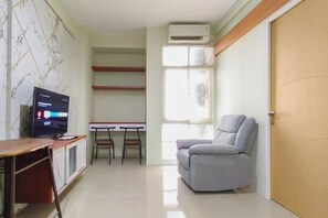 Una habitación con televisión, escritorio, sillas, sofá y aire acondicionado.