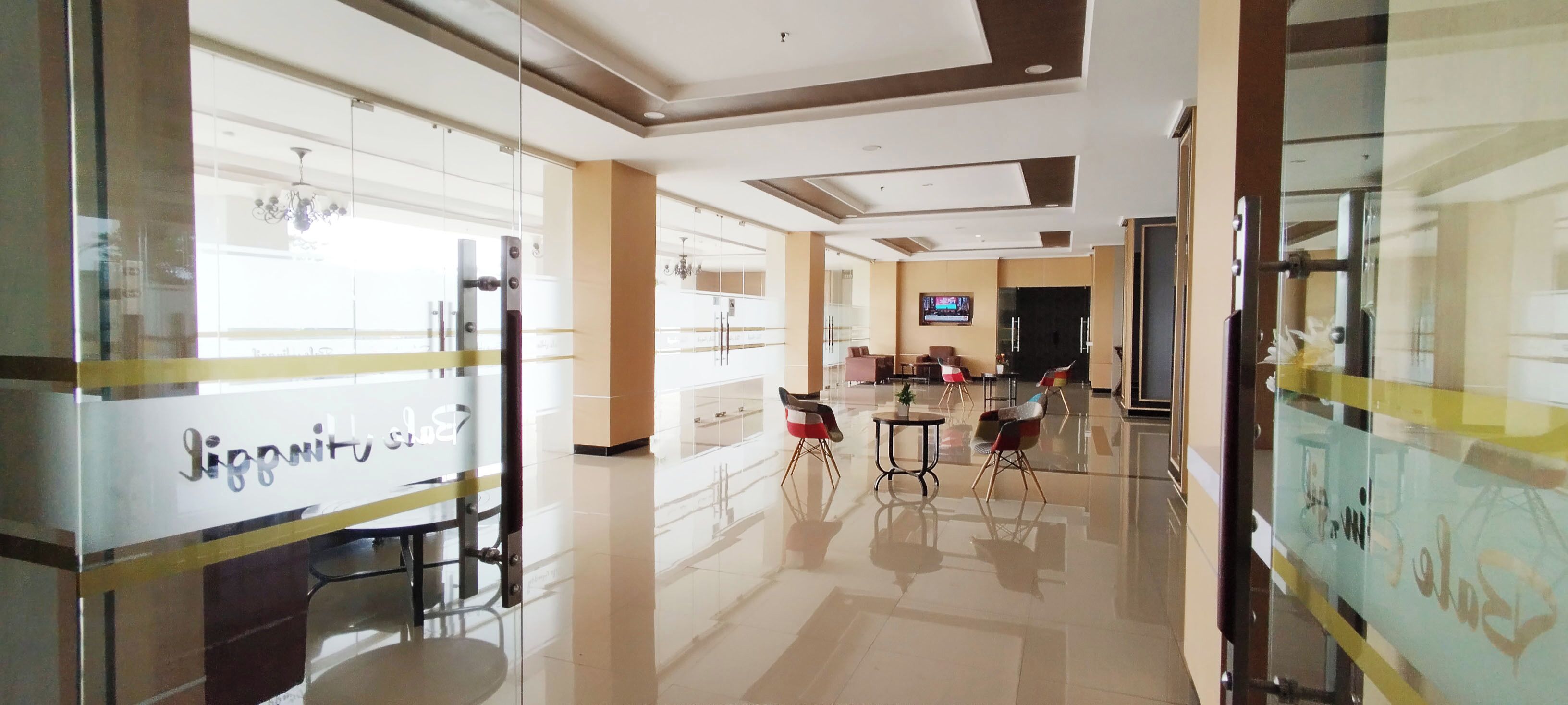 A hotel lobby with a glass partition, a reception desk, and a seating area with chairs and a table.