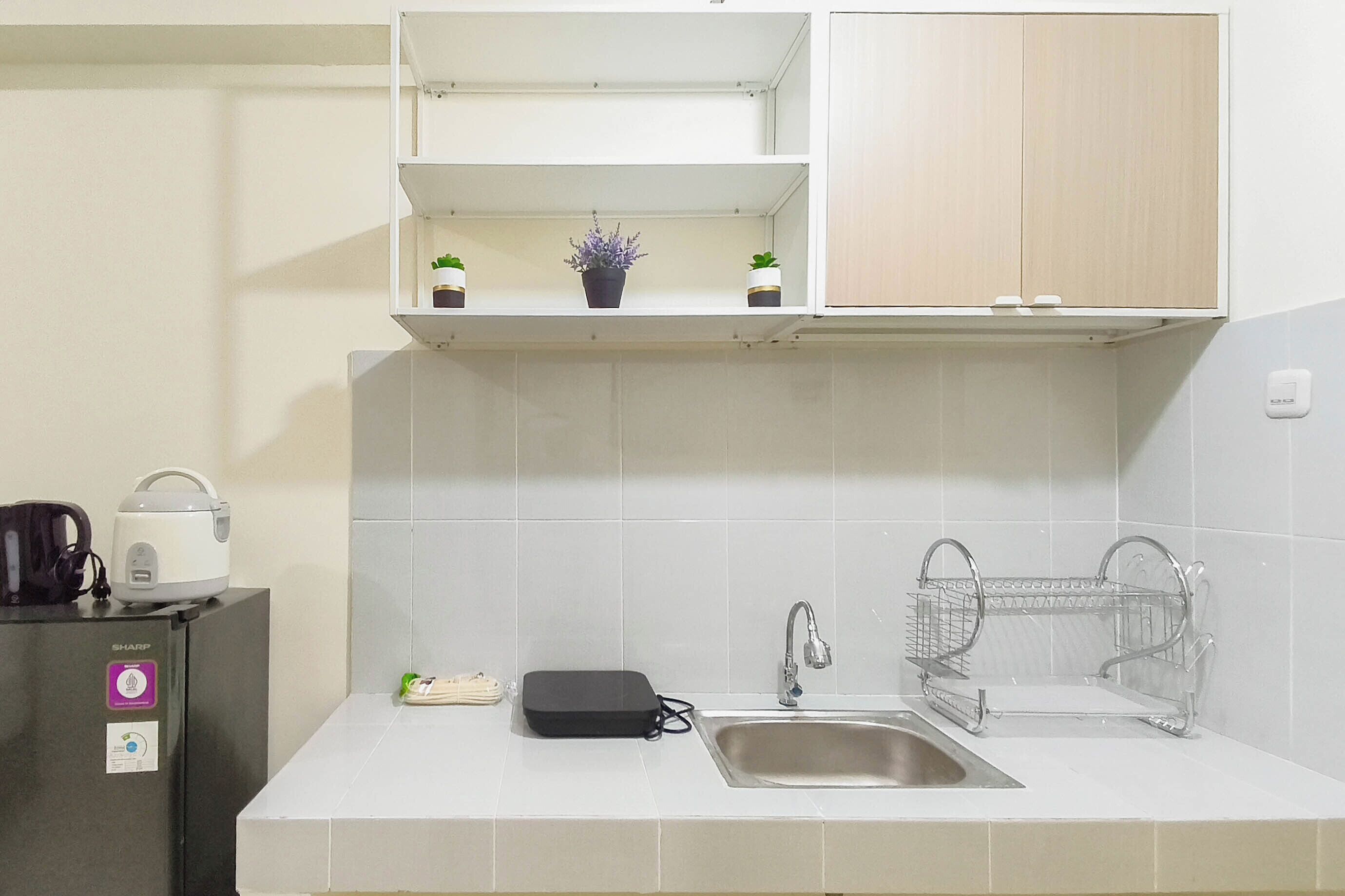 A kitchen with a sink, a kettle, a small refrigerator, and a dish rack.