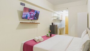 Quarto de hotel com uma cama, televisão na parede, escrivaninha com cadeira e banheiro visível por uma porta aberta.