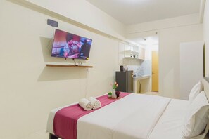 Une chambre d’hôtel avec un lit, un téléviseur fixé au mur, un bureau avec une chaise et une salle de bain visible à travers une porte ouverte.
