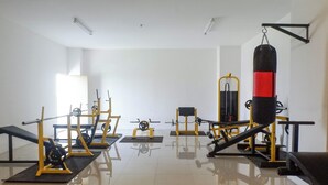 Uma academia com diversos equipamentos de exercício, incluindo máquinas de musculação, um banco e um saco de pancadas.