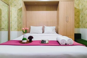 A neatly made bed with white linens, a pink bedspread, and a small vase with pink flowers. - Studio Minimalist And Comfortable At Bale Hinggil Apartment (Surabaya)