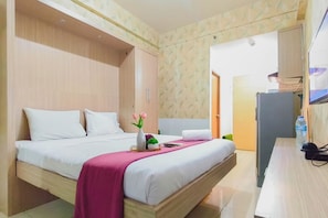 Una habitación de hotel con cama, escritorio, refrigerador y puerta que da a otra habitación.