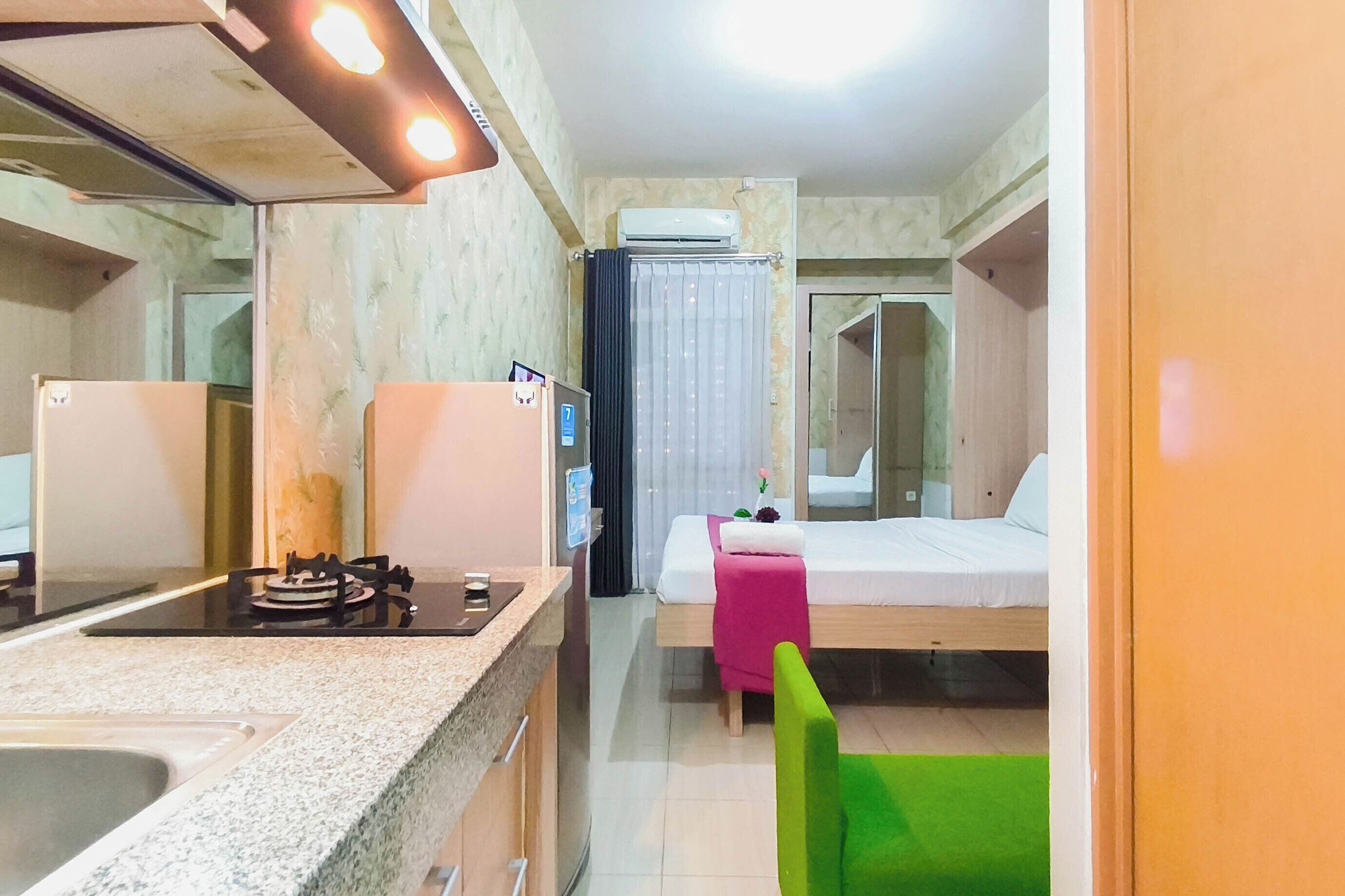 Ein kleines Hotelzimmer mit Küchenzeile, einem Bett, einem Tisch und einem grünen Stuhl.