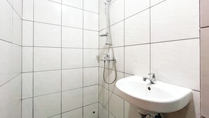 A bathroom with white tiled walls, a shower with a handheld showerhead, and a white sink with a faucet. - Good Deal Studio (No Kitchen) Bandaraya - Tallasa City Makassar Apartment (Makassar)
