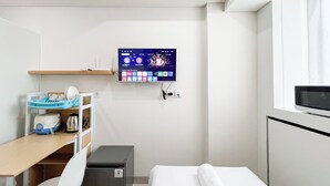 A hotel room with a bed, a desk with a computer, a TV mounted on the wall, and a small storage unit. - Good Deal Studio (No Kitchen) Bandaraya - Tallasa City Makassar Apartment (Makassar)