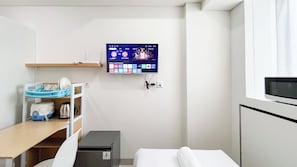 Ein Hotelzimmer mit Bett, Schreibtisch mit Computer, Wandfernseher und einer kleinen Ablagemöglichkeit.