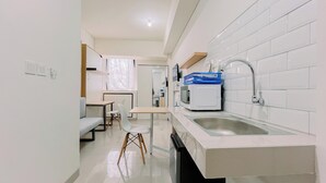 A modern kitchen with a built-in microwave, a sink, and a dining area with a table and chairs. - Warm And Comfy Studio Apartment (No Kitchen) Bandaraya - Tallasa City Makassar (Makassar)