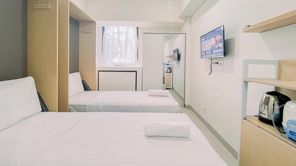 Habitación de hotel con dos camas, televisión, hervidor de agua y cafetera.