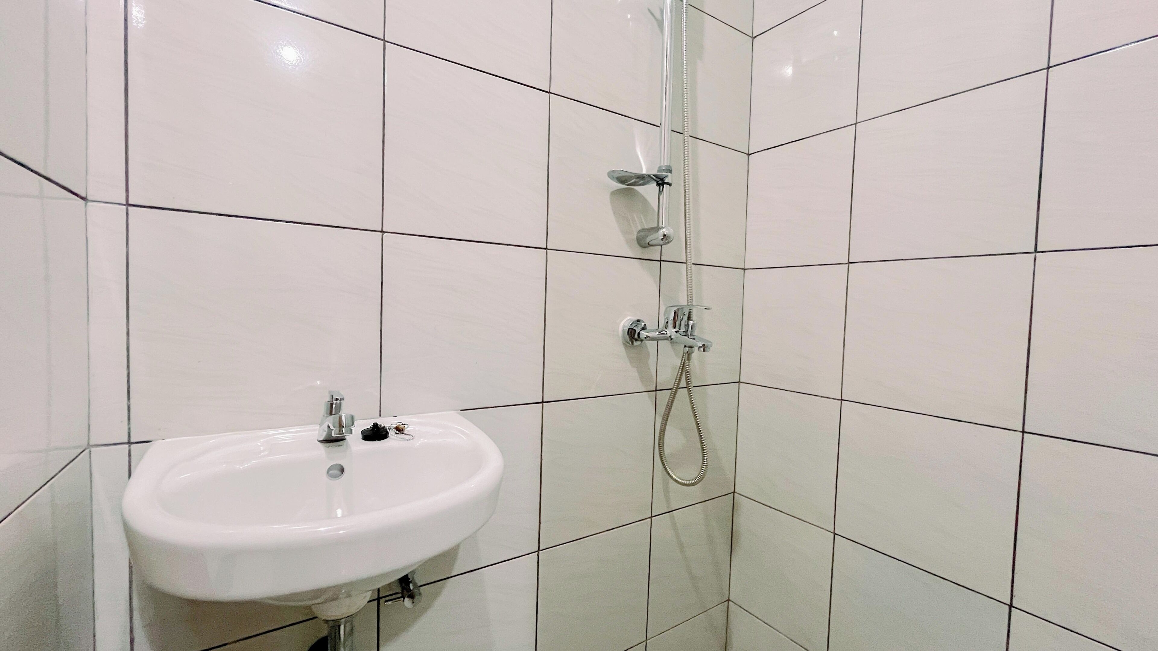 A bathroom with a white sink, a shower with a handheld showerhead, and tiled walls.