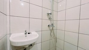 Un baño con lavamanos blanco, ducha con cabezal de ducha de mano y paredes de azulejos.