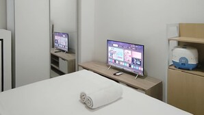Ein Hotelzimmer mit Bett, Fernseher auf einem Schrank, Spiegel und kleinem Tisch mit Handtuch.