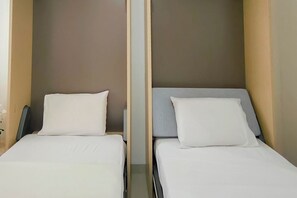 Zwei Einzelbetten mit weißer und grauer Bettwäsche, eine neutrale Wandfarbe und ein Holz-Kopfbrett.