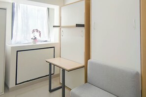 Ein Zimmer mit Fenster, Schreibtisch, Stuhl und Kleiderschrank.