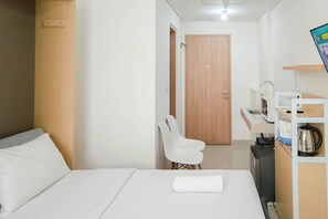 Ein Hotelzimmer mit einem Bett, einem weißen Stuhl, einer Holztür, einer Küchenzeile und einem kleinen Schrank.
