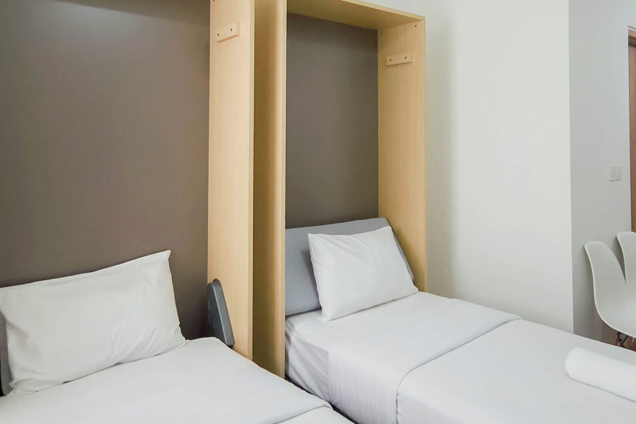 A hotel room with two beds, a chair, and a wooden partition.
