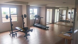 A gym with a treadmill, weight bench, and barbell rack. - Homey And Neat Studio Room At Apartment Belmont Residence Puri (Jakarta)