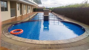 A swimming pool with a lifebuoy, surrounded by a building with a glass roof and a concrete deck. - Homey And Neat Studio Room At Apartment Belmont Residence Puri (Jakarta)
