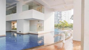 A modern building with a swimming pool, glass railings, and a view of surrounding high-rise buildings. - Tranquil 2Br Direct Access To Mall At Benson Supermall Mansion Apartment (Surabaya)
