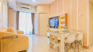 A modern hotel room with a sofa, a TV, a dining table with chairs, and a large window with curtains. - Tranquil 2Br Direct Access To Mall At Benson Supermall Mansion Apartment (Surabaya)