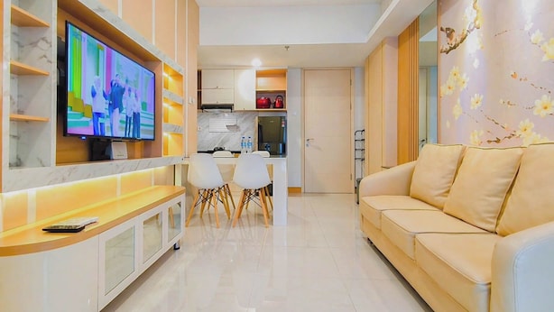 A modern living room with a flat-screen TV, a sofa, a dining area with chairs, and a kitchen in the background. - Tranquil 2Br Direct Access To Mall At Benson Supermall Mansion Apartment (Surabaya)