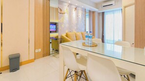 A modern dining area with a glass table, white chairs, and a yellow sofa. - Tranquil 2Br Direct Access To Mall At Benson Supermall Mansion Apartment (Surabaya)