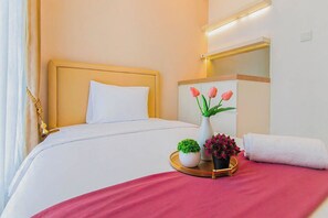 A hotel room with a bed, a bedside table with a vase of flowers, and a mirror above the bed. - Tranquil 2Br Direct Access To Mall At Benson Supermall Mansion Apartment (Surabaya)