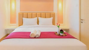 A hotel room with a bed, pillows, a tray with towels, and a vase with flowers. - Tranquil 2Br Direct Access To Mall At Benson Supermall Mansion Apartment (Surabaya)