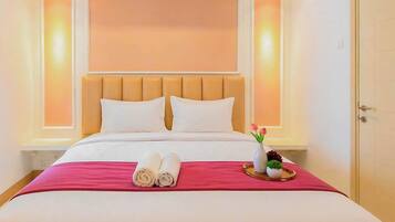 A hotel room with a bed, pillows, a tray with towels, and a vase with flowers.