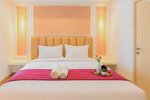 A hotel room with a bed, pillows, a tray with towels, and a vase with flowers. - Tranquil 2Br Direct Access To Mall At Benson Supermall Mansion Apartment (Surabaya)