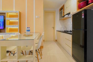 A compact kitchen with a refrigerator, a dining table with chairs, a TV, and a water dispenser. - Tranquil 2Br Direct Access To Mall At Benson Supermall Mansion Apartment (Surabaya)