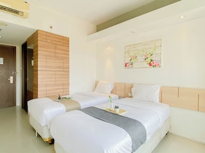 A hotel room with two beds, a wooden headboard, a wall-mounted artwork, and a door. - Comfortable Studio (No Kitchen) At Bogor Icon Apartment (Bogor)