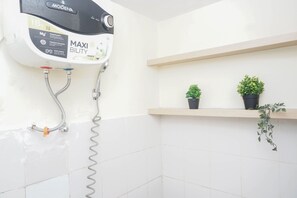 A bathroom with a wall-mounted shower head, a toilet, and two potted plants on a shelf. - Best Price Studio At Bogor Valley Apartment (Bogor)
