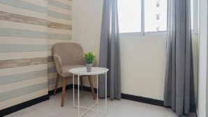 Quarto com parede listrada, uma cadeira, uma mesa pequena com uma planta e uma janela com cortinas.