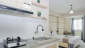 A modern kitchen with a gas stove, a sink, and a built-in oven. There is a bed with a Uniland mattress, a window with curtains, and a hanging light fixture. - Best Price Studio At Bogor Valley Apartment (Bogor)
