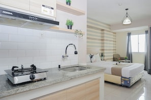 Cozinha moderna com fogão a gás, pia e forno embutido. Há uma cama com colchão Uniland, janela com cortinas e luminária pendente.