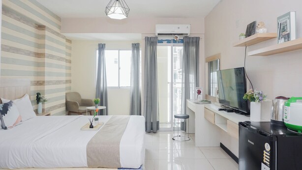 A hotel room with a bed, bedside table, TV, refrigerator, and a desk with a chair. - Best Price Studio At Bogor Valley Apartment (Bogor)